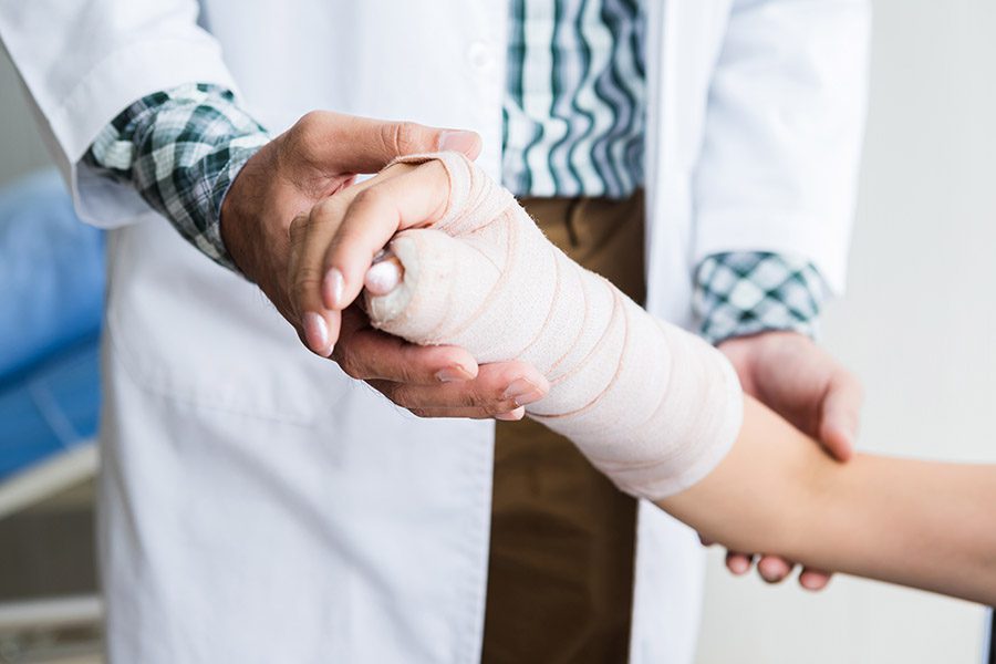 Group Accident Insurance - Woman Holding Up her Broken Arm with a Doctor Adding a Cast