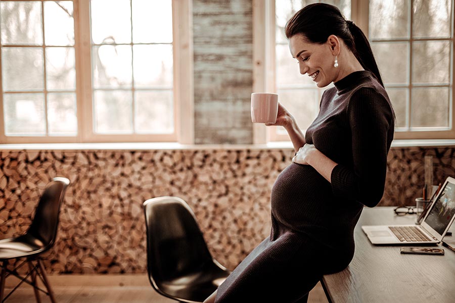 Employee Benefits - Pregnant Businesswoman Admires Her Baby Bump, Drinking Coffee in a Modern Office Space
